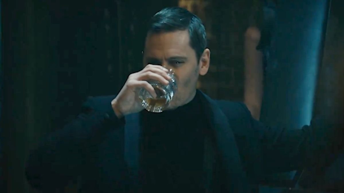 Tek Knight takes a sip of dark liquor while wearing an all black suit in the boys